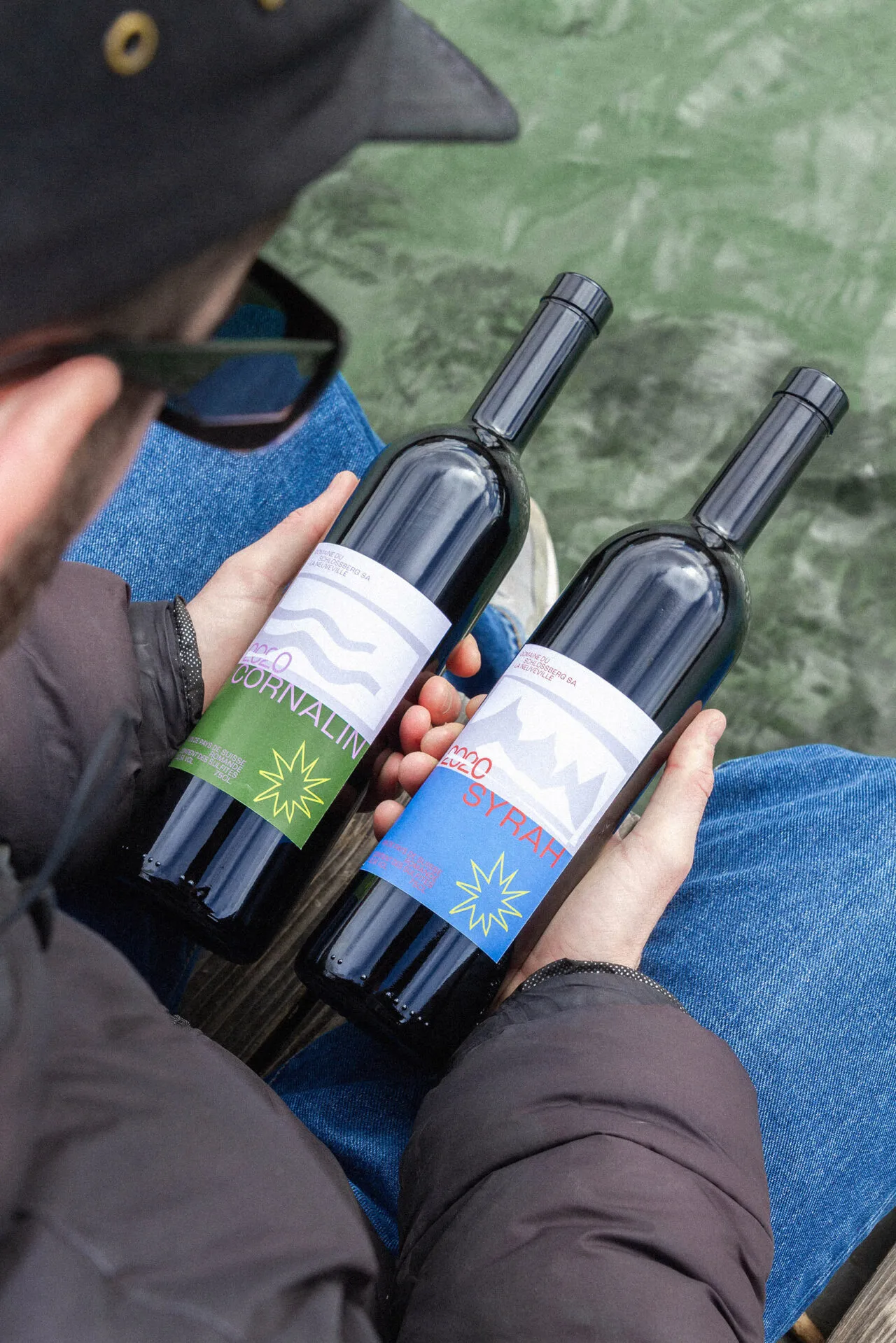 Deux bouteilles de Cornalin et de Syrah du Domaine du Schlossberg tenues au-dessus du lac